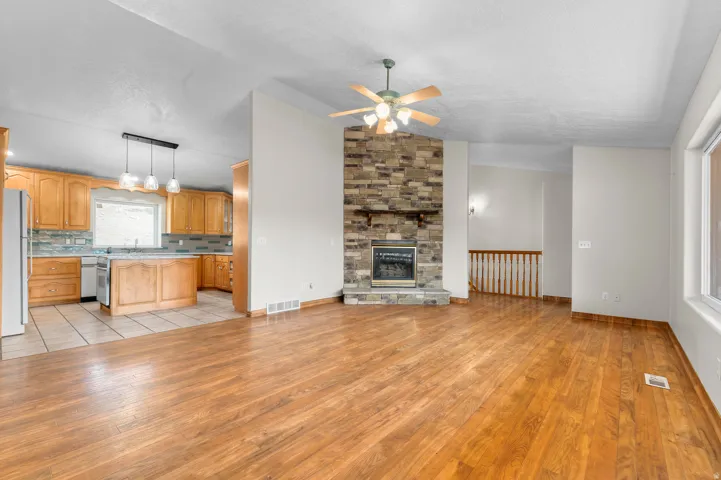 Open-concept living space with wood-finish flooring, a stone-front fireplace, and a ceiling fan