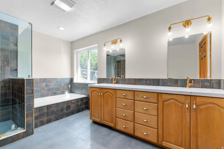 Spacious bathroom featuring a dual vanity, built-in soaking tub, walk-in shower with glass enclosure, and tiled flooring