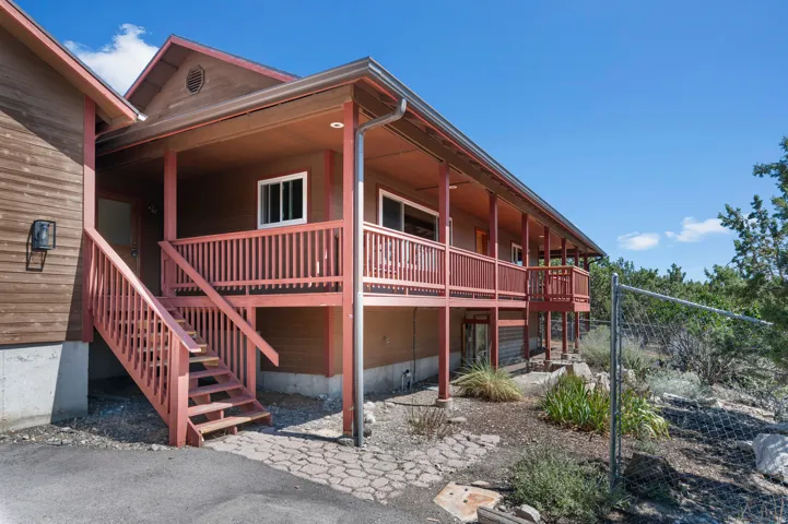 Wood-sided exterior featuring an elevated covered porch, red-painted wood railings, red-painted wood stairs, and a partial chain-link fence