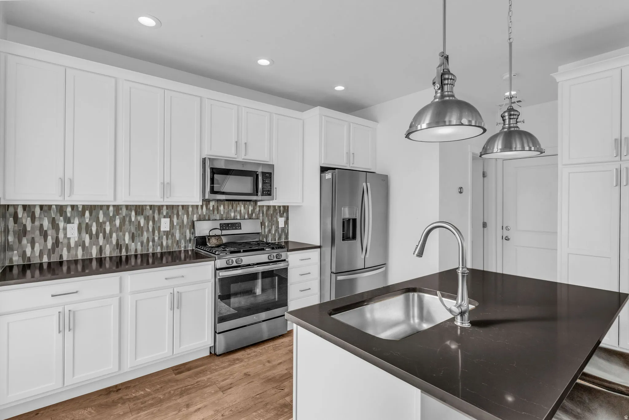 Kitchen featuring white shaker cabinetry, stainless steel appliances, dark countertops, a mosaic tile backsplash, and wood-finish flooring
