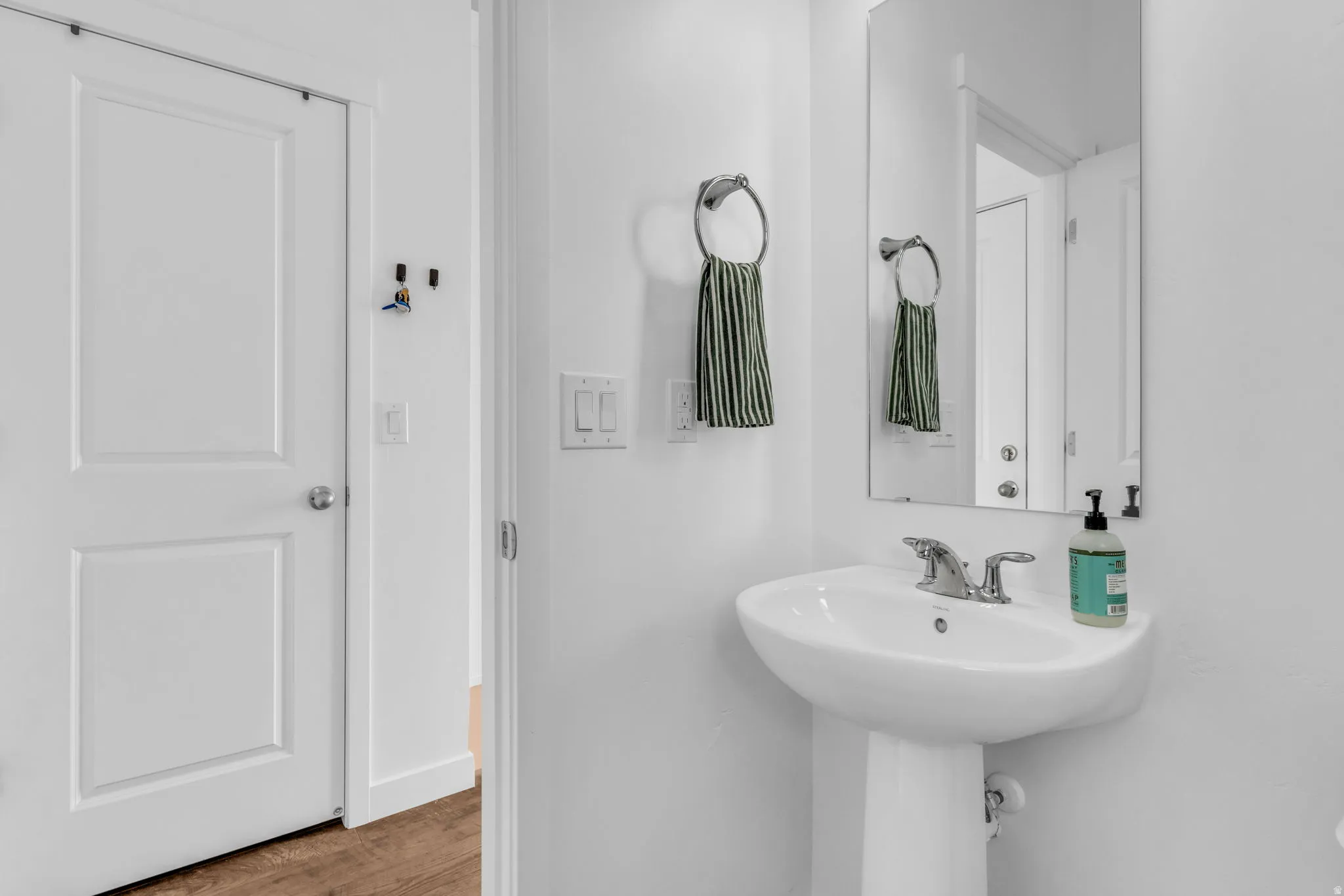 Pedestal sink with chrome faucet, wall-mounted rectangular mirror, and wood-finish flooring