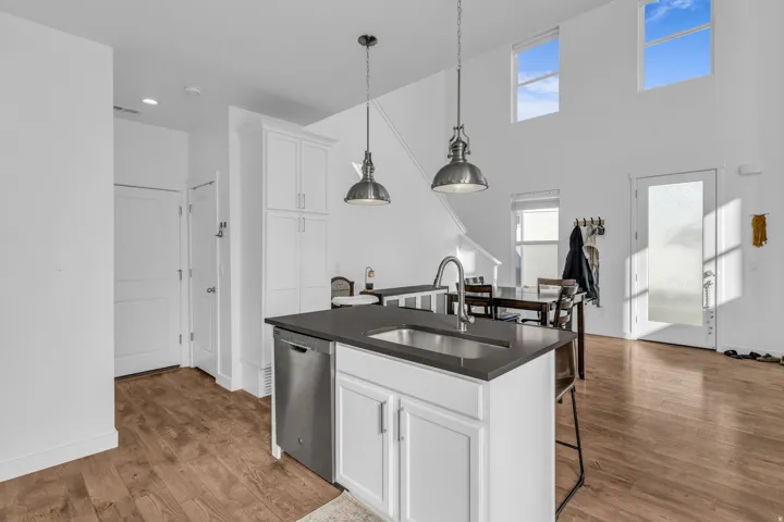 White cabinetry with dark countertops, stainless steel dishwasher, wood-finish flooring, and high ceilings