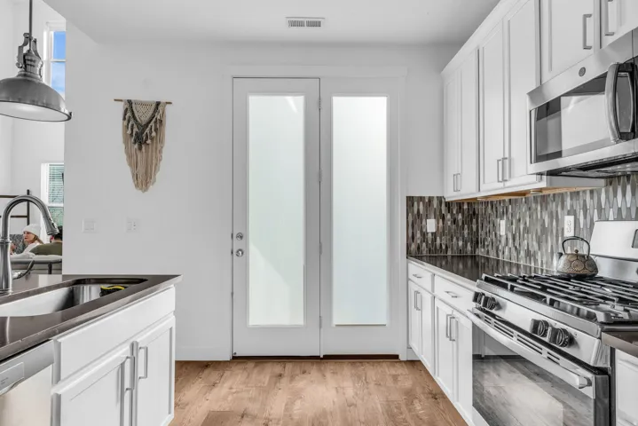 White shaker-style cabinetry with stainless steel appliances, dark countertops, and a mosaic tile backsplash
