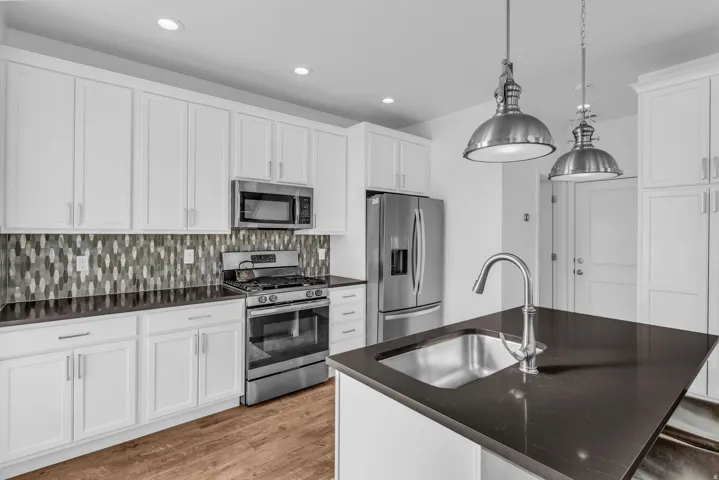 Kitchen featuring white shaker cabinetry, stainless steel appliances, dark countertops, a mosaic tile backsplash, and wood-finish flooring