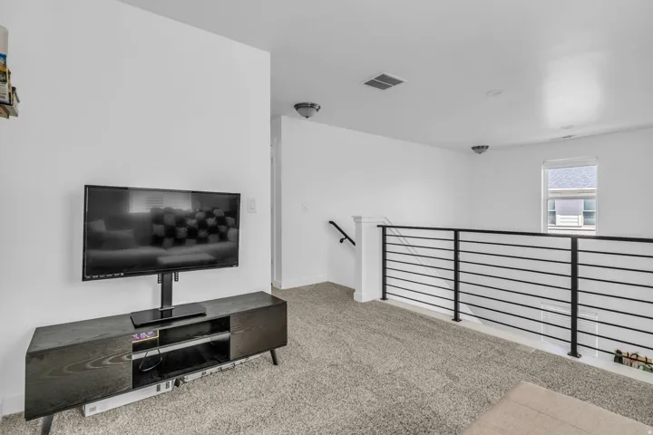 Carpeted upper-level space featuring a contemporary horizontal metal railing, a single window, and a wall-mounted light fixture