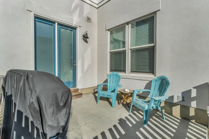Private patio space featuring a concrete surface, a glass-panel door with blue trim, and a window with blinds