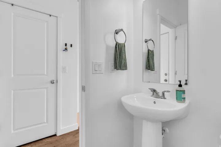 Pedestal sink with chrome faucet, wall-mounted rectangular mirror, and wood-finish flooring