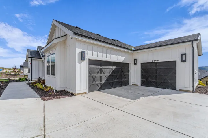 White vertical siding exterior with black gabled roof, dual black garage doors, and concrete driveway