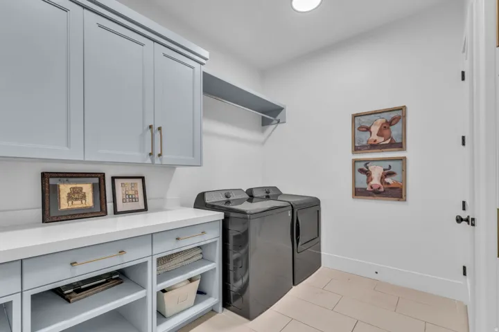 Light blue cabinetry with gold-tone hardware, white countertop, open shelving, and light-toned tile flooring