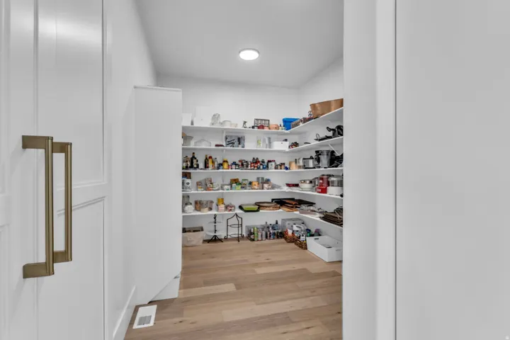 Walk-in pantry featuring extensive built-in shelving, wood-finish flooring, and recessed lighting
