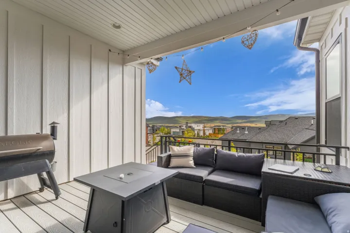 Covered exterior deck with composite decking, white vertical siding, black metal railing, and a mountain backdrop