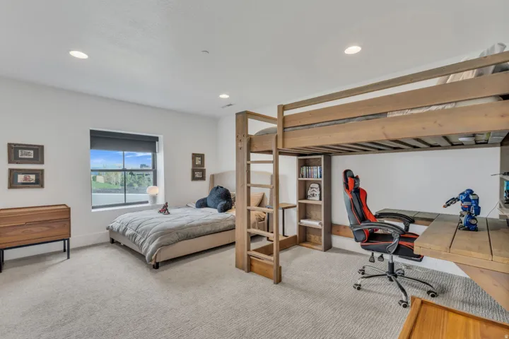 Recessed lighting, light-toned carpeting, a large window, and a built-in wooden bunk bed with integrated desk