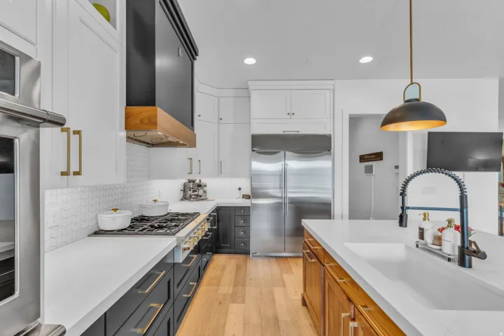 Gourmet kitchen featuring a built-in oven, stainless steel appliances, white cabinetry, dark lower cabinetry, and a kitchen island with an integrated sink