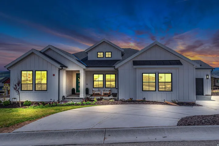 Board and batten siding, black-framed windows, a covered entry, a concrete driveway, and a dark shingle roof