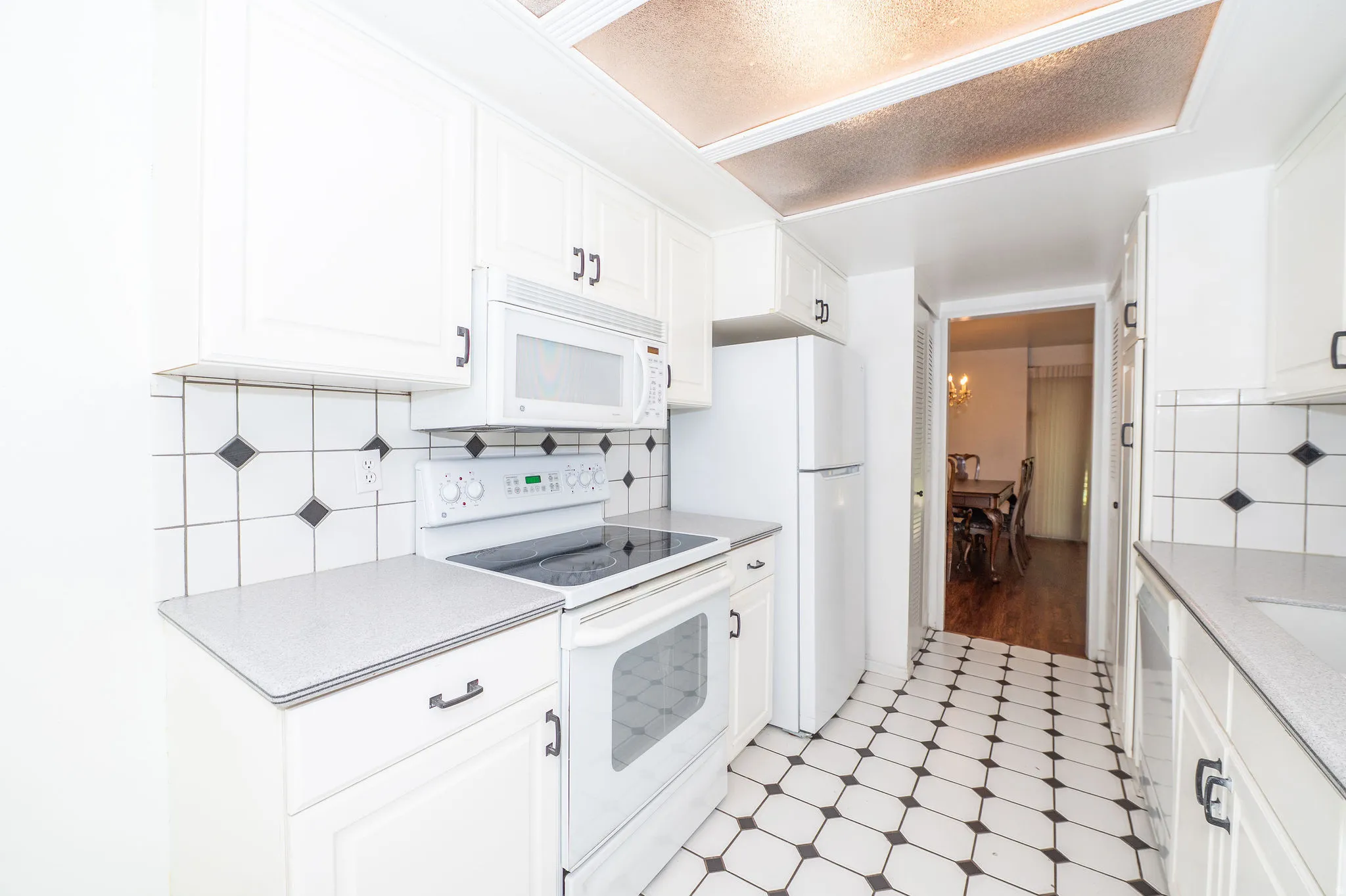 White cabinetry with dark hardware, a white tile backsplash with black diamond accents, and a white electric range with a built-in microwave