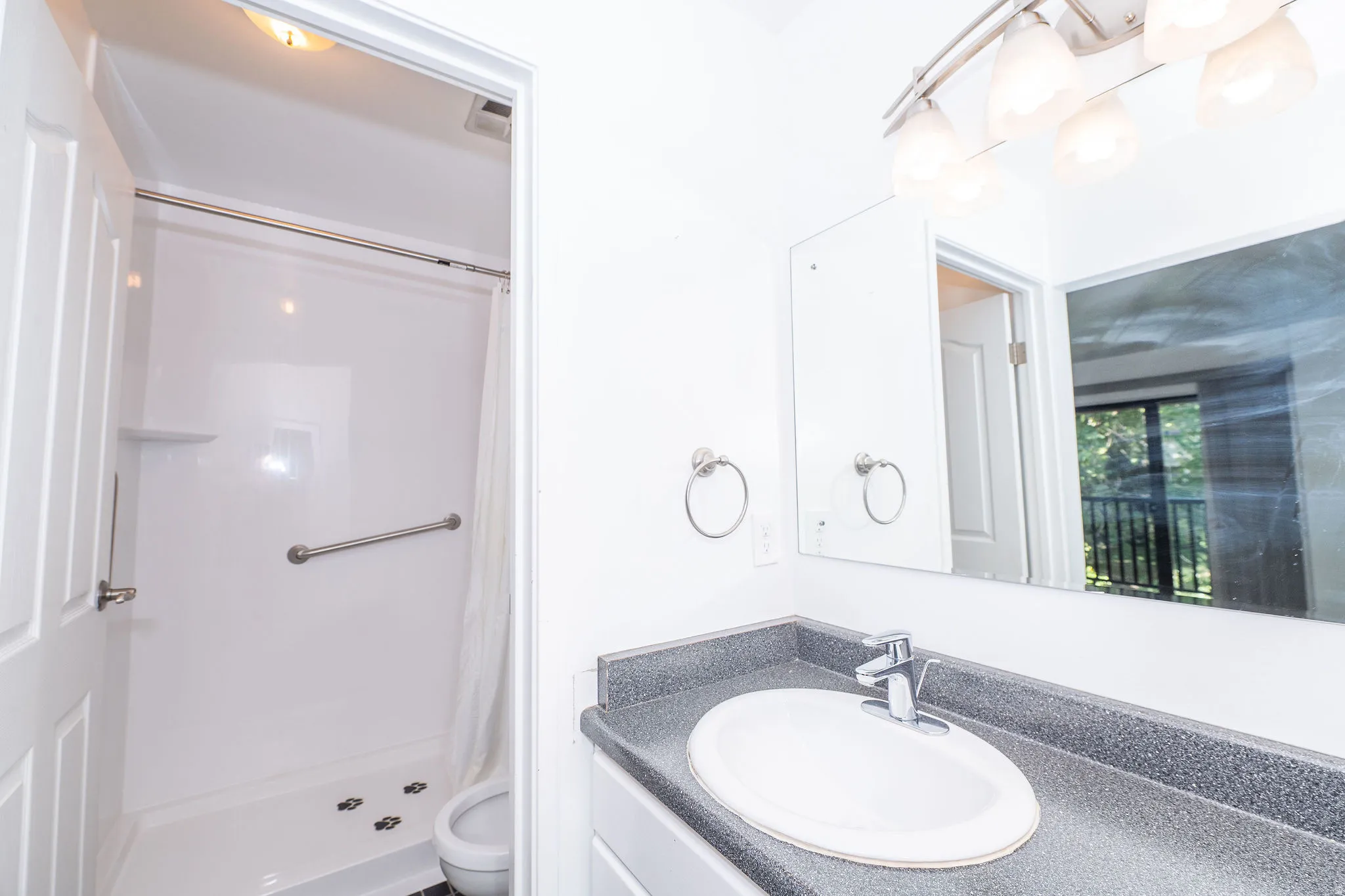 Bathroom with a built-in shower featuring a grab bar, a vanity with an integrated sink, and a wall-mounted light fixture