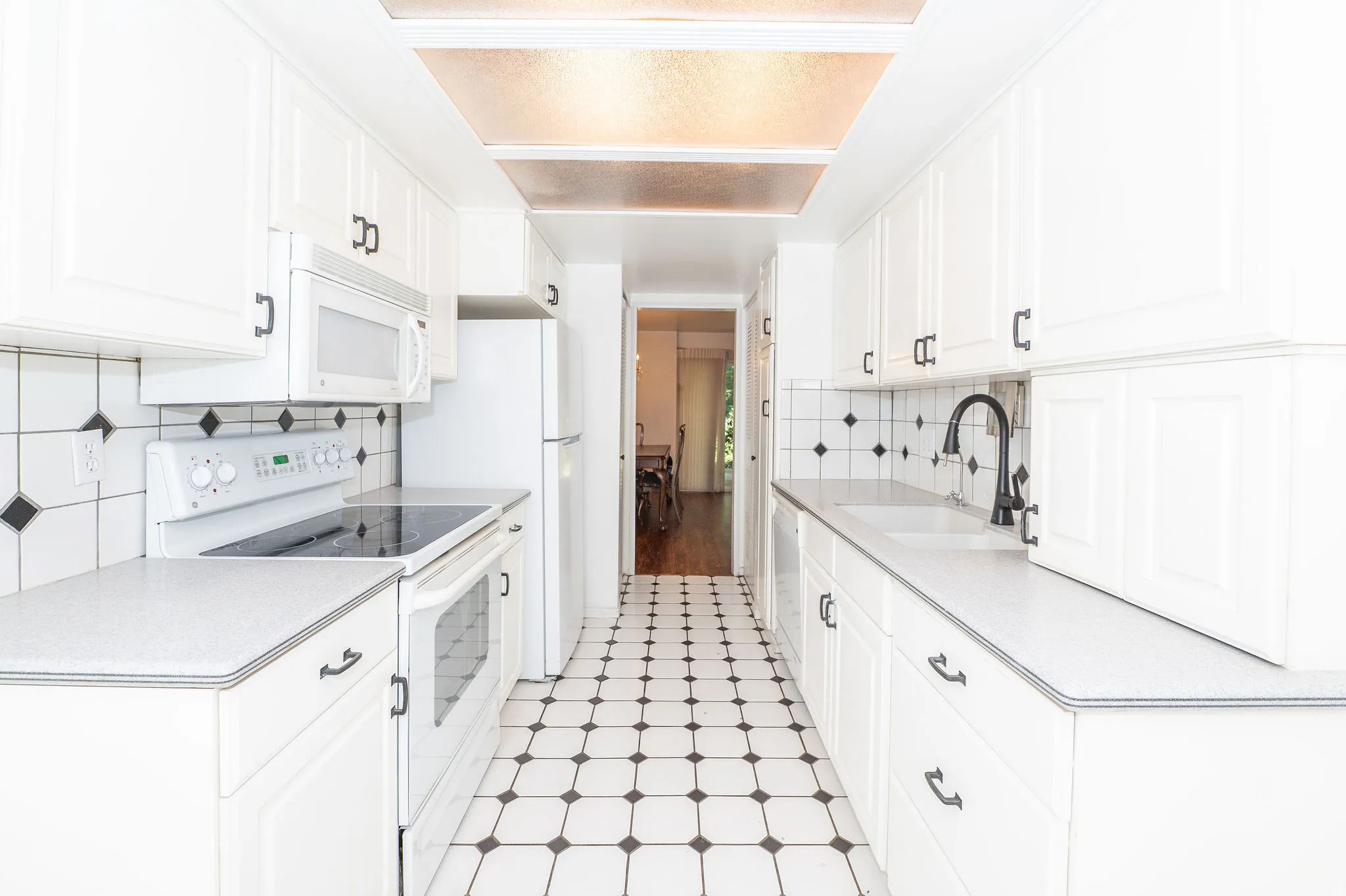 Galley kitchen featuring white cabinetry, black and white floor tiles, a drop-in sink with a matte black faucet, and a tile backsplash