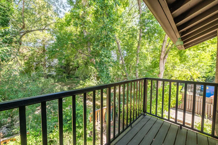 Balcony featuring composite decking and black metal railings, overlooking a tree-lined natural setting