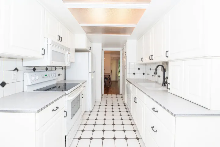 Galley kitchen featuring white cabinetry, black and white floor tiles, a drop-in sink with a matte black faucet, and a tile backsplash