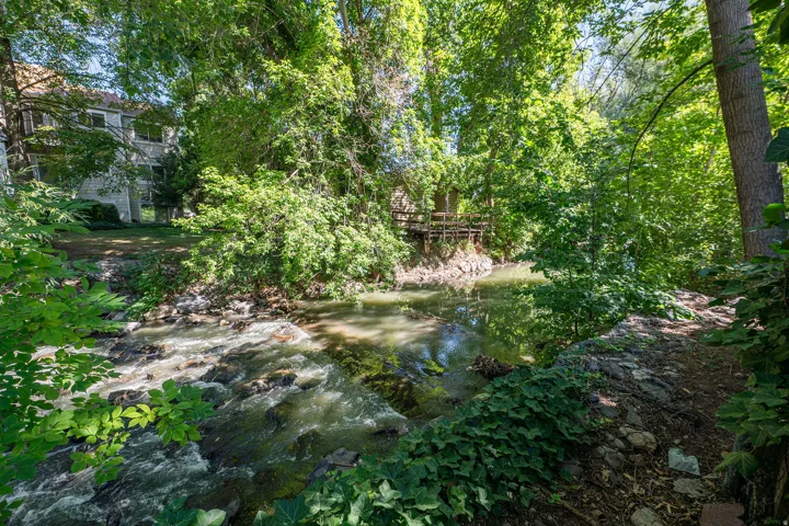 Wooded riverfront setting with a visible two-story structure, lush foliage, and a wooden bridge structure