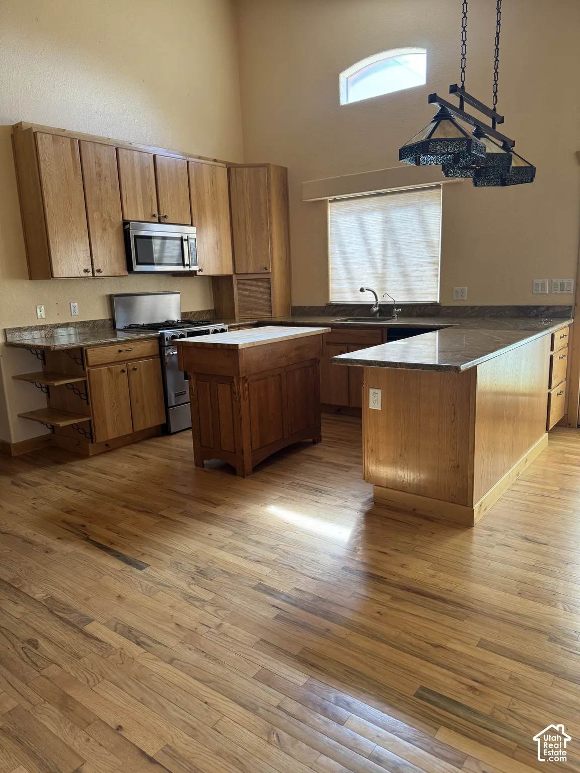 Kitchen featuring wood-finish flooring, custom wooden cabinetry, a built-in microwave, an arched window, and a decorative pendant light fixture