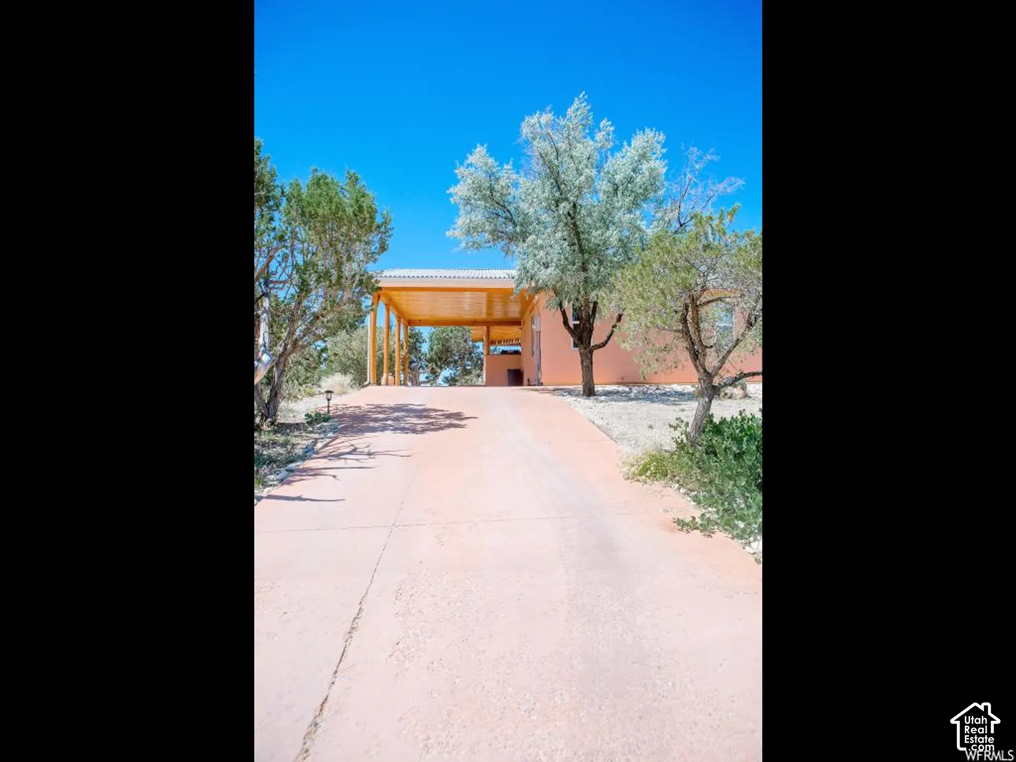 Paved driveway with an open carport featuring wood support beams and a clear roof