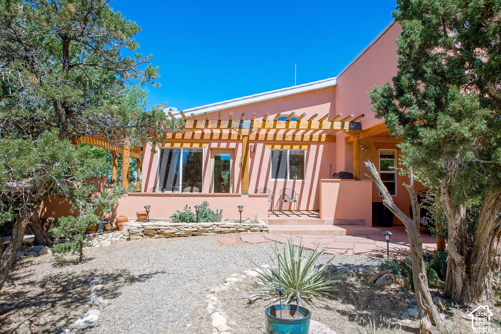 Stucco exterior with a wood pergola, multiple large windows, and a stone patio