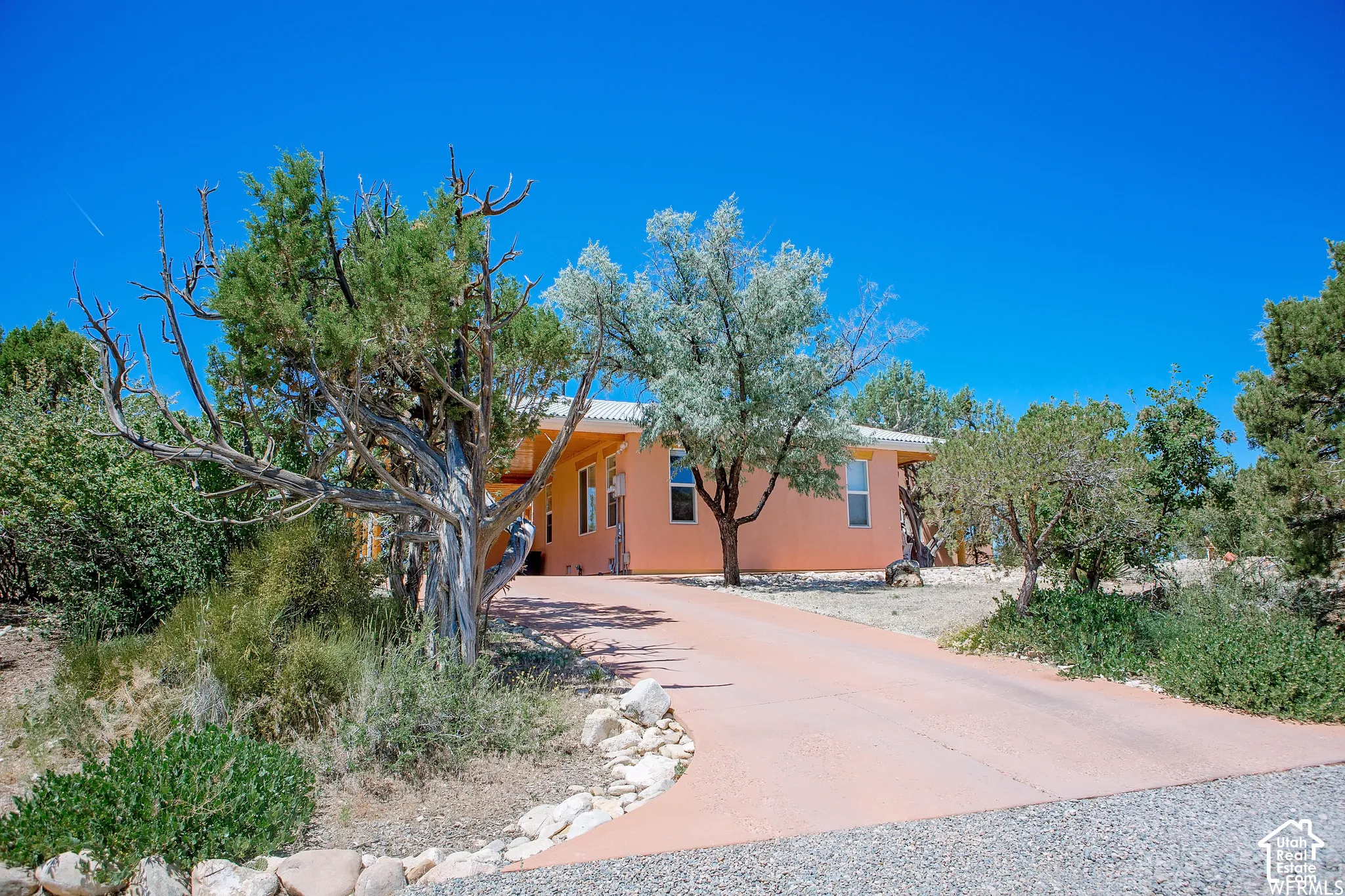 Orange stucco exterior with a white trim roofline, accented by natural rock landscaping and mature trees