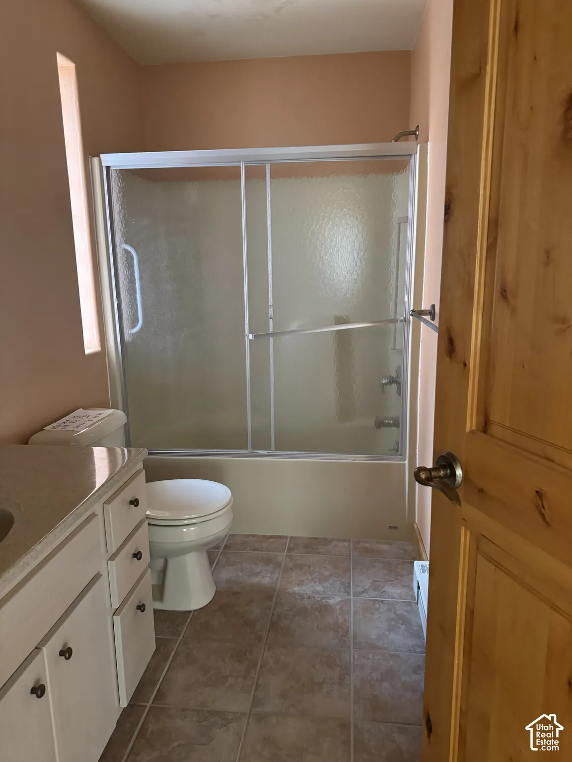 Bathroom featuring a full vanity with an integrated sink, a toilet, a bathtub with a sliding glass enclosure, and a narrow vertical window