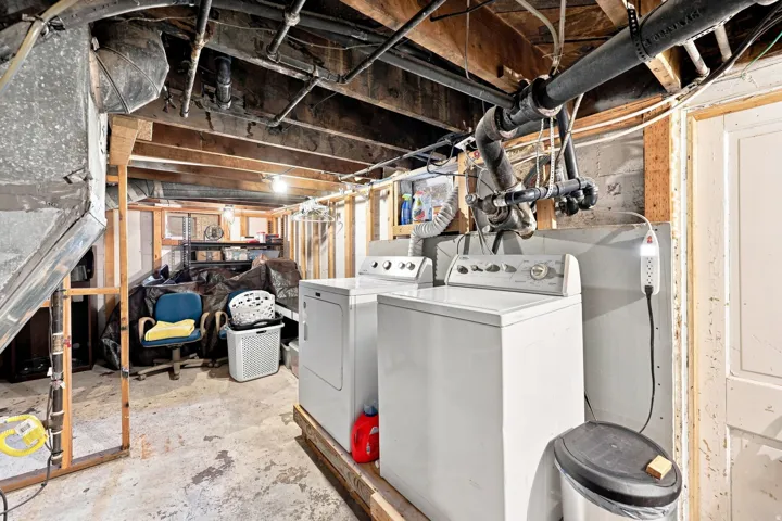 Basement laundry area featuring exposed ceiling joists and concrete flooring