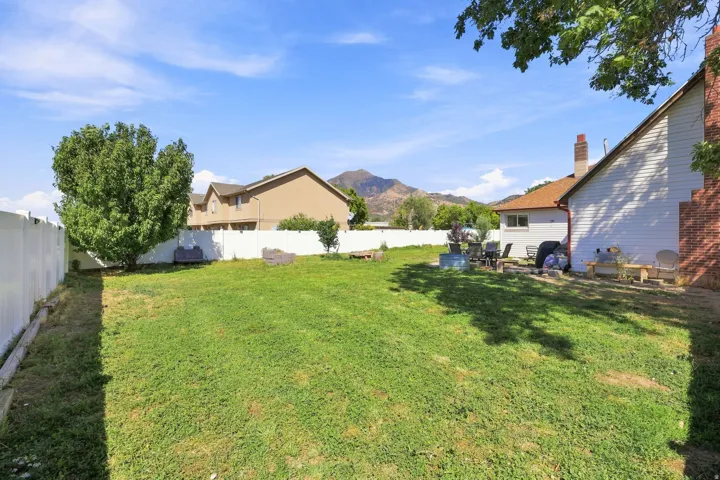 Expansive grassy yard with a white privacy fence and a mature shade tree