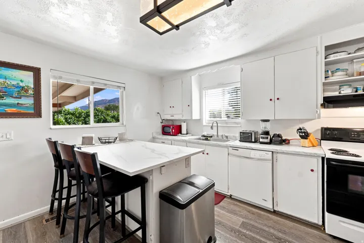 White cabinetry, white countertops, wood-finish flooring, a stainless steel sink, and a black range