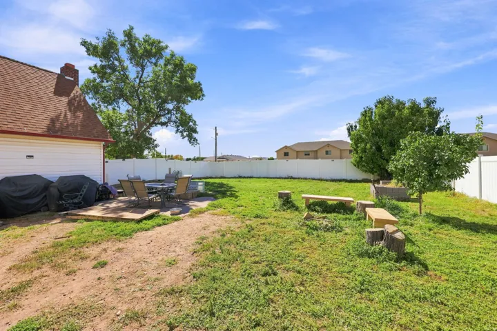 Expansive backyard featuring a white vinyl privacy fence, mature trees, and a concrete patio space