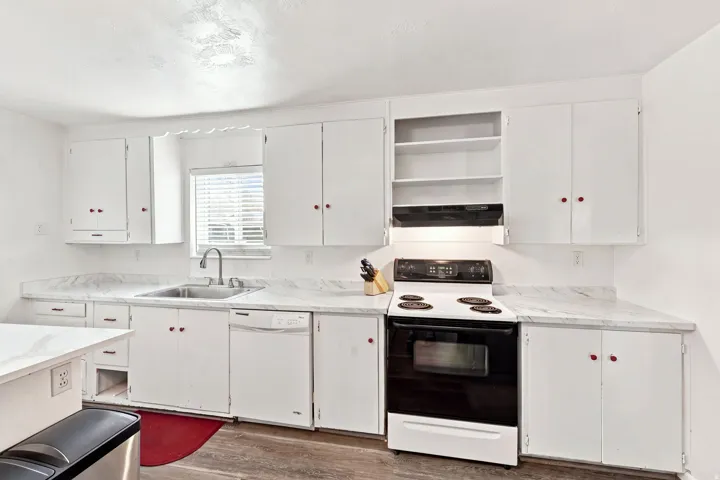Kitchen featuring white cabinetry, light-toned countertops, a stainless steel sink with a gooseneck faucet, a white dishwasher, and a white range with a black cooktop
