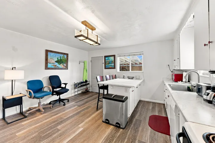 Wood-finish flooring throughout, white cabinetry with red knob accents, light-colored countertops, stainless steel sink with pull-down faucet, and a contemporary ceiling light fixture