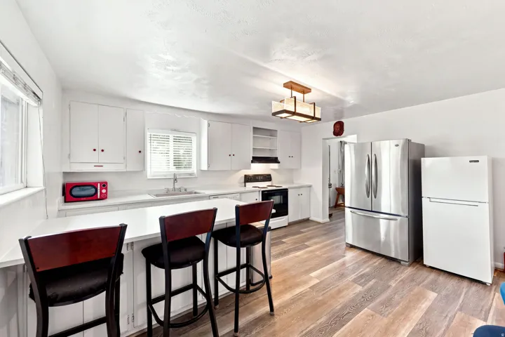 Kitchen featuring white cabinetry, wood-finish flooring, a stainless steel refrigerator, a built-in oven, and a breakfast bar