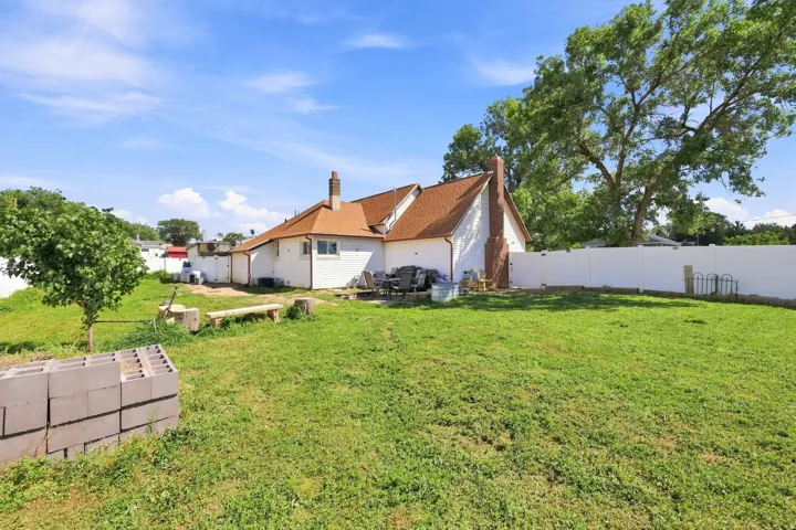 Expansive backyard featuring a white vinyl fence, mature trees, and a brick chimney exterior