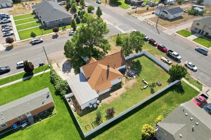 Expansive lot with a pitched shingle roof, mature trees, and a white privacy fence