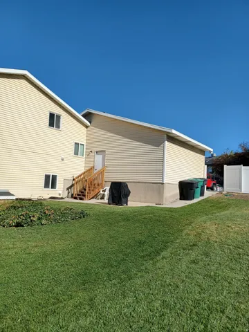 Expansive lawn area with a concrete patio, wooden staircase, and mature landscaping