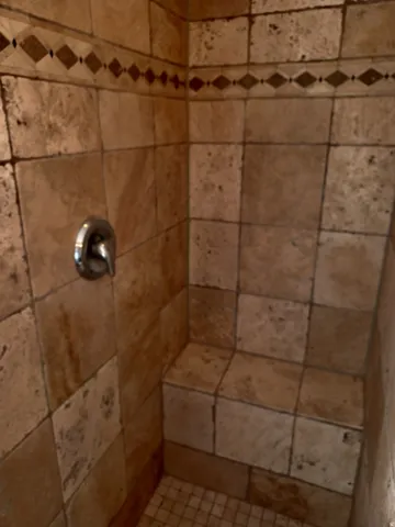 Tiled shower with a built-in bench, decorative tile accent band, and a polished chrome shower valve