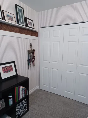 Bi-fold closet doors, textured wall covering, a built-in display shelf with cork backing, and neutral-toned carpeting