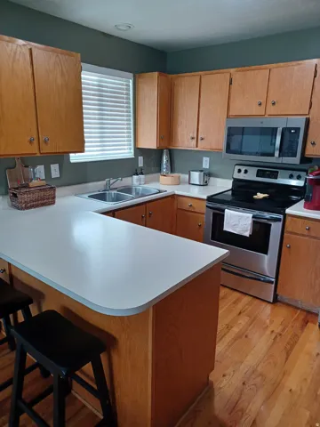 Hardwood flooring, wood-finish cabinetry, stainless steel appliances, laminate countertops, and a double basin sink