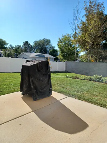 Concrete patio with a grass lawn, white privacy fencing, and a concrete block wall