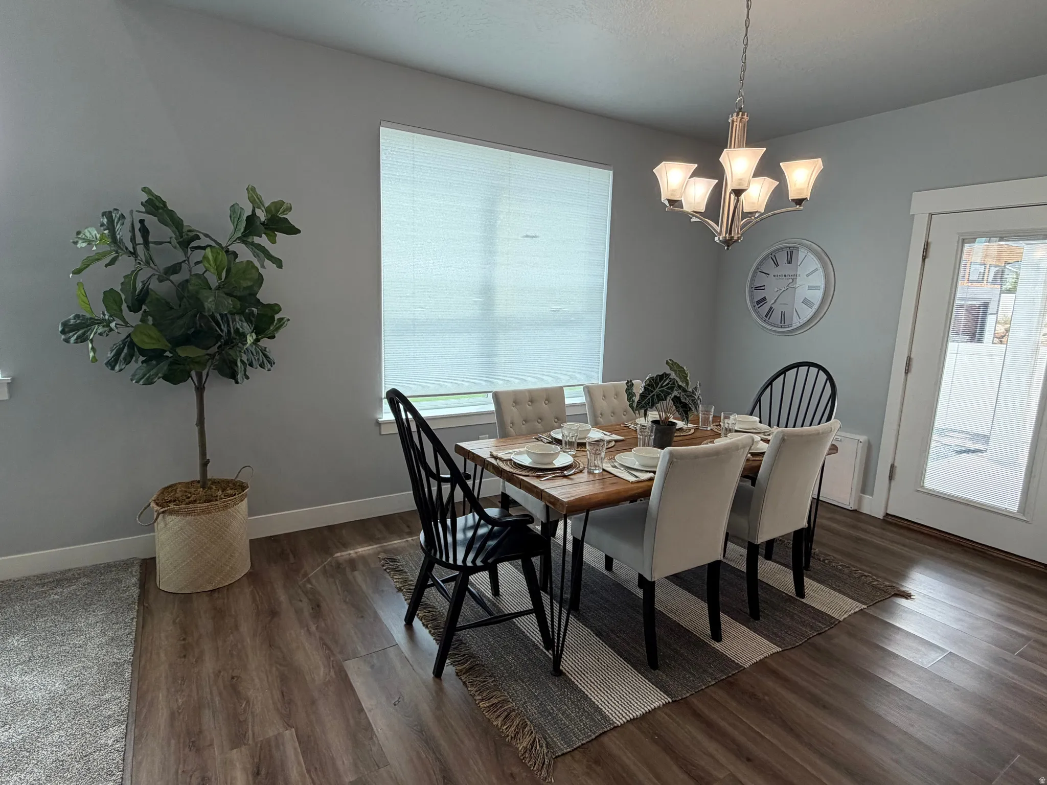 Wood-finish flooring, single window with blinds, overhead chandelier, light gray walls, and a glass-paneled door
