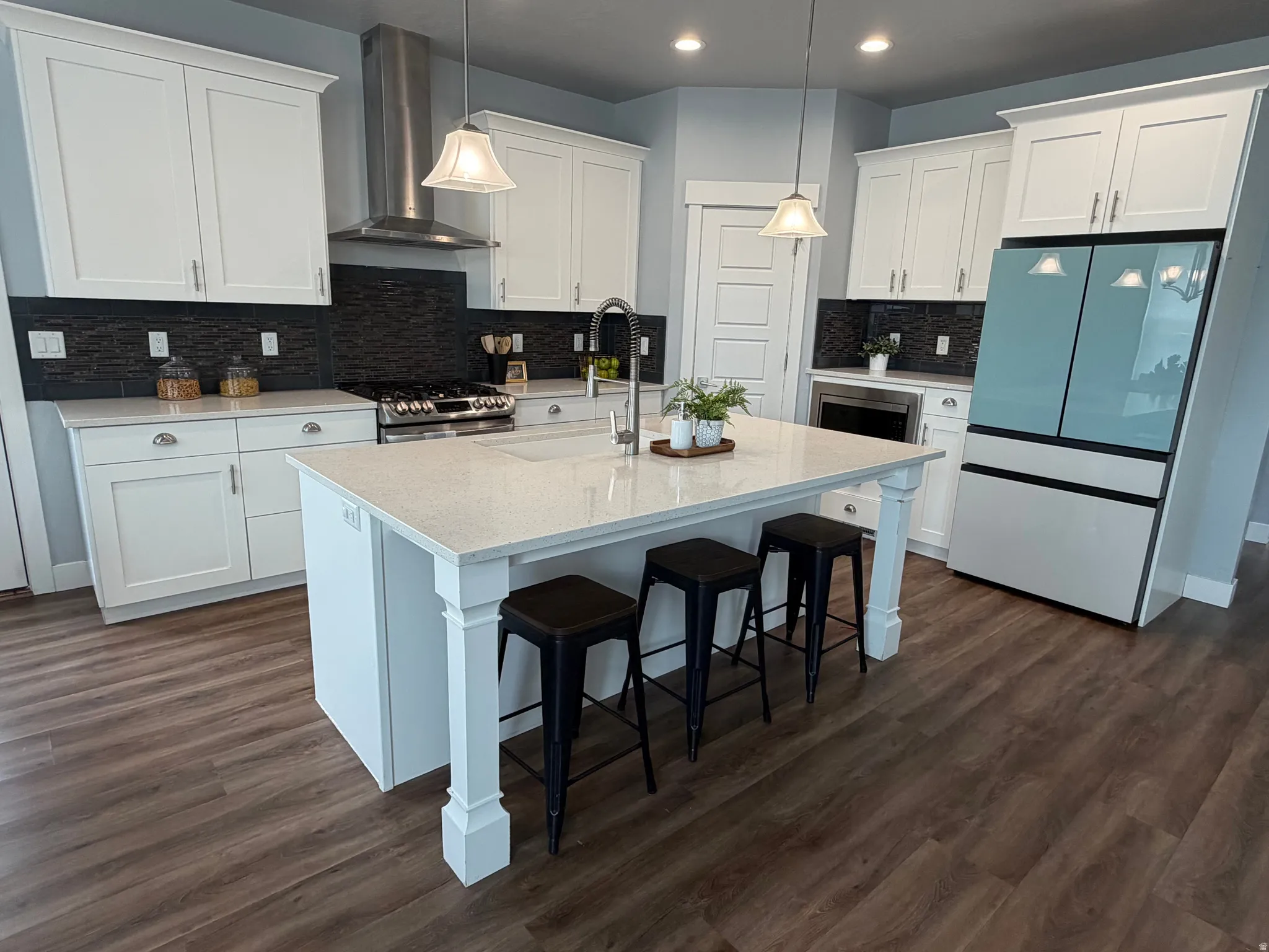 Kitchen featuring white cabinetry, wood-finish flooring, a central island with a light-toned countertop, black tile backsplash, and stainless steel appliances