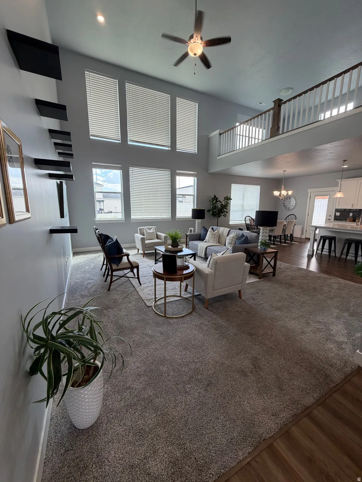Living area with a two-story ceiling, multiple tall windows, and an upper-level interior balcony with white spindle railing