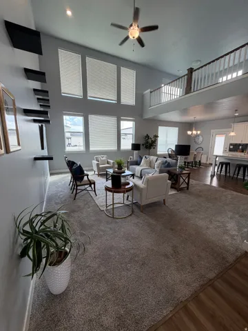 Living area with a two-story ceiling, multiple tall windows, and an upper-level interior balcony with white spindle railing