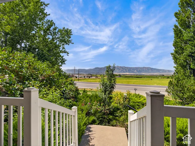 White railings with a broad mountain backdrop, expansive green fields, and mature trees