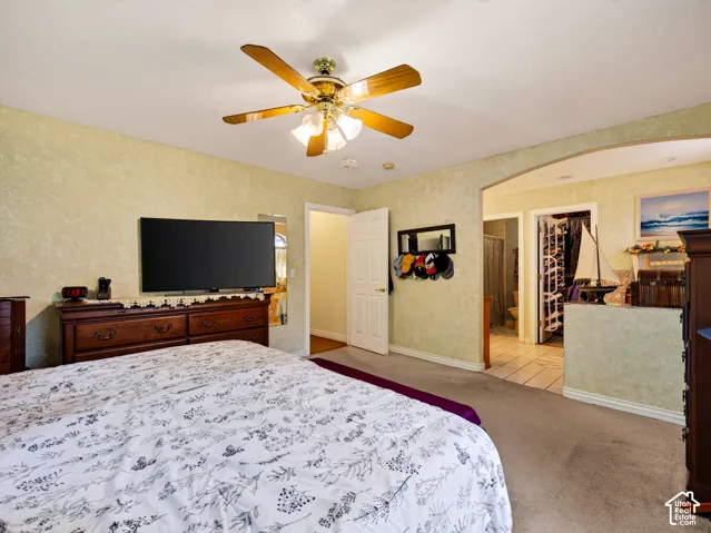 Primary bedroom with ceiling fan, integrated lighting, arched doorway, carpet flooring, tiled flooring, and a standard white door