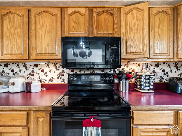 Wood cabinetry, black over-the-range microwave, black electric range, and red countertops